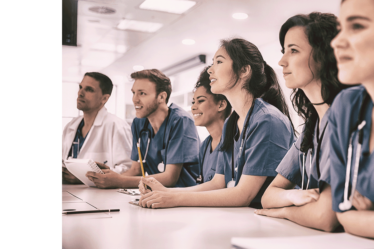 Students in scrubs listening to a lecture at a desk