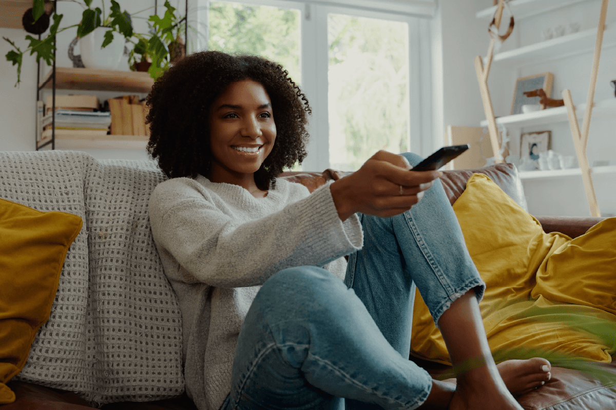 Woman pointing a TV remote, Go to Streaming TV Advertising Growth Is Outpacing Expectations—Is Your Brand Ready?