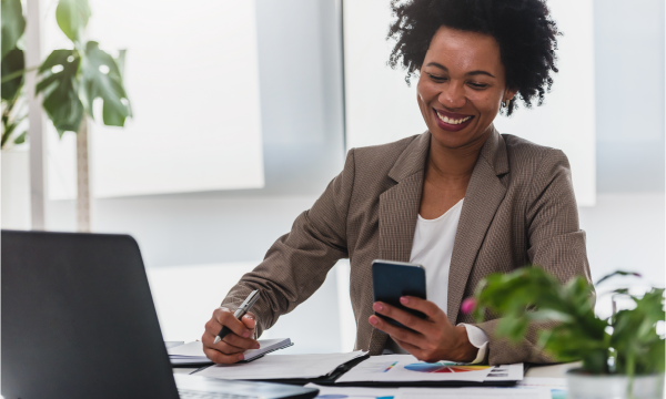 Woman sitting in front of her laptop using her mobile device