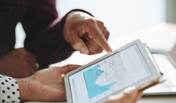 A person pointing at a tablet screen with graphs