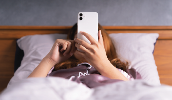 Someone waking up in a city apartment stretching in bed, grabbing their phone for the first morning scroll.