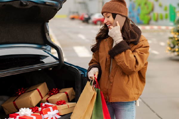 A woman on her phone while taking holiday presents out of a car trunk