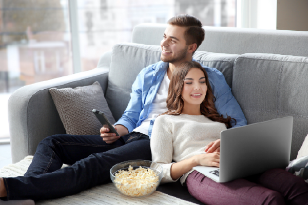 A couple sitting on the couch on a laptop and watching TV